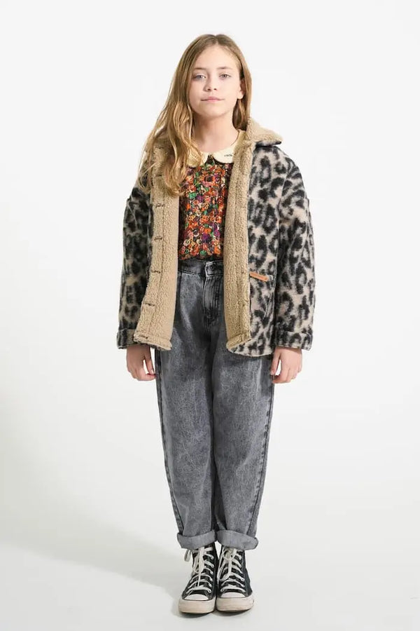 Niña con pantalones unisex grises, blusa de flores multicolor y chaqueta con estampado de animal print con borreguito.