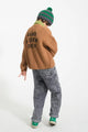 Niño con cárdigan marrón de punto con botones de Piupiuchick y texto estampado “Band & Crew Only”, y con pantalón denim negro lavado con logo bordado en bolsillo trasero izquierdo 
