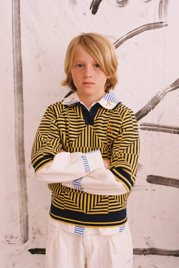 Niño con polo de True Artist de color azul marino y estampado de caleidoscopios de color amarillo.